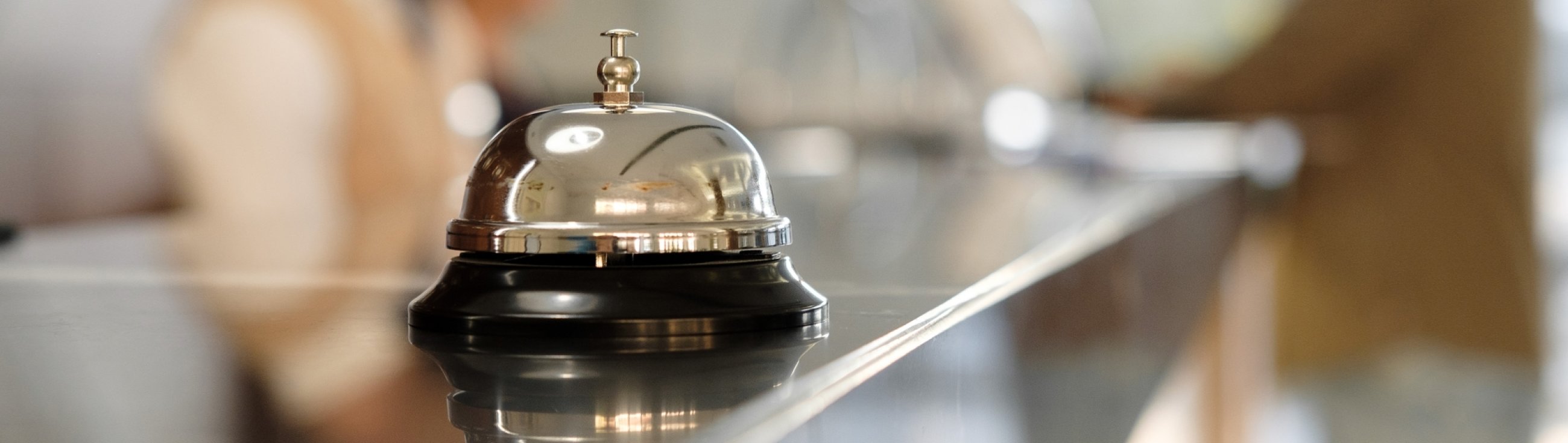 Modern luxury Hotel Reception Counter desk with Bell. Service Bell locating at reception. Silver Call Bell on table, Receptionists and customer on background. Сheck in hotel. Concept.